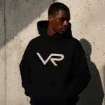 A stylish man wearing a premium black and gold foil Vie Riche graphic t-shirt and matching track pants.