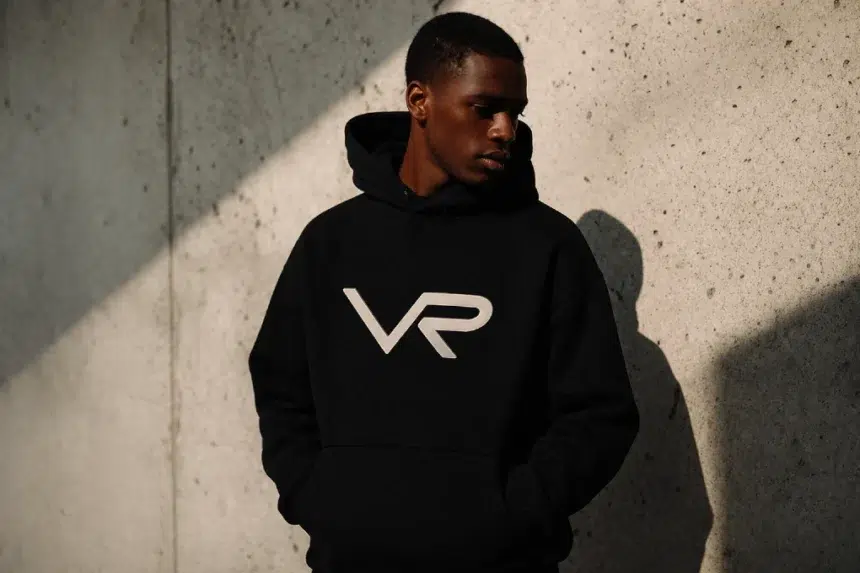 A stylish man wearing a premium black and gold foil Vie Riche graphic t-shirt and matching track pants.