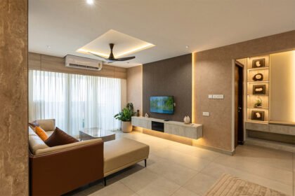 Modern minimalist living room with a neutral color palette, featuring a floating TV unit, recessed cove lighting, and a beige L-shaped sofa.